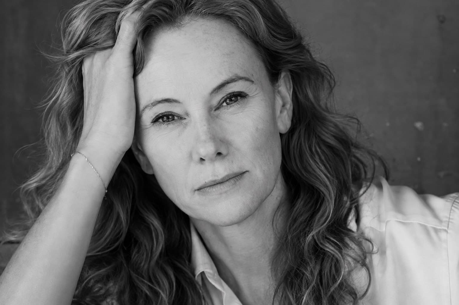 Milan Murray in a light button-down shirt, photographed in black and white, her hand resting in her hair.