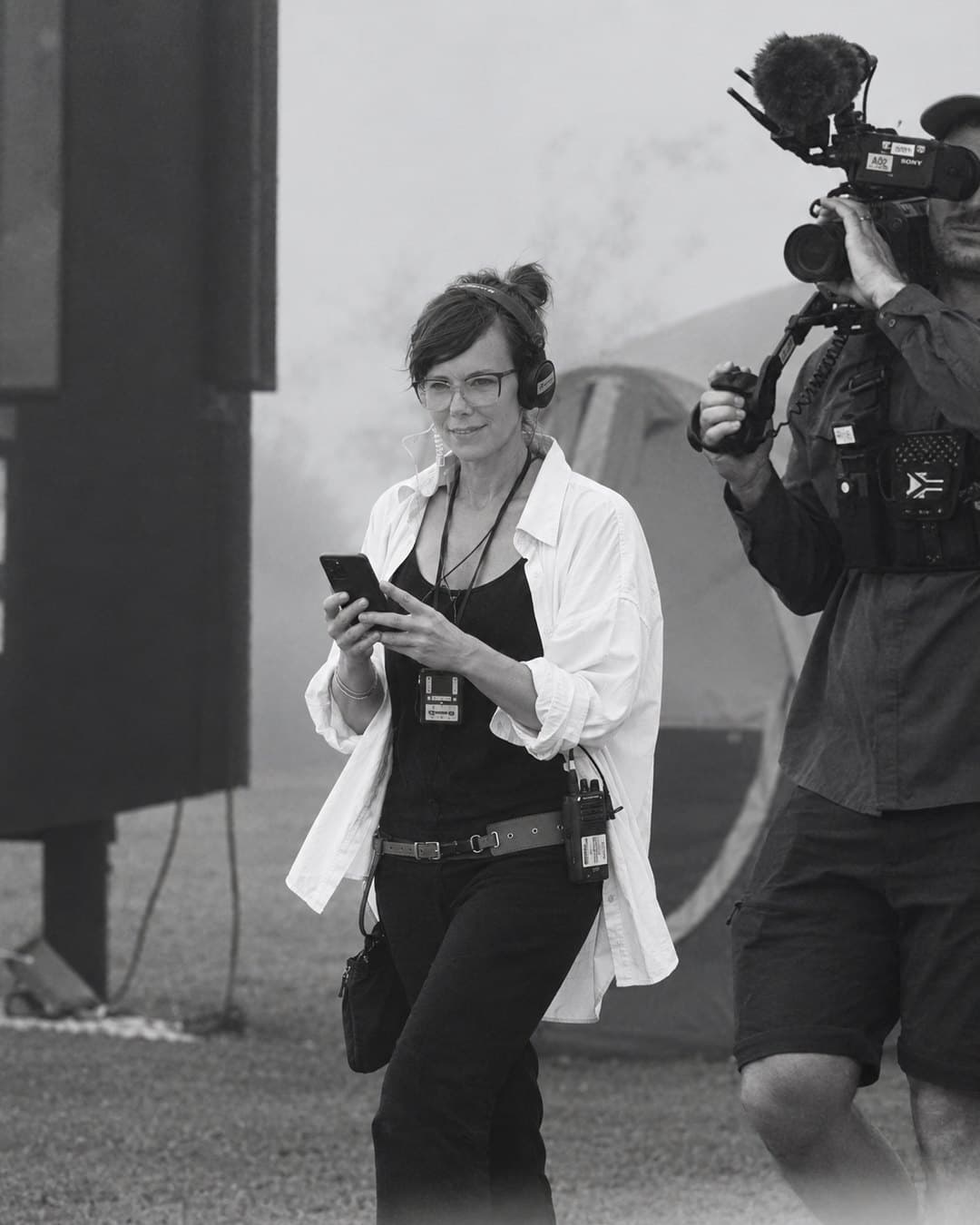 Milan Murray on a production set with headphones and a walkie-talkie, photographed in black and white.