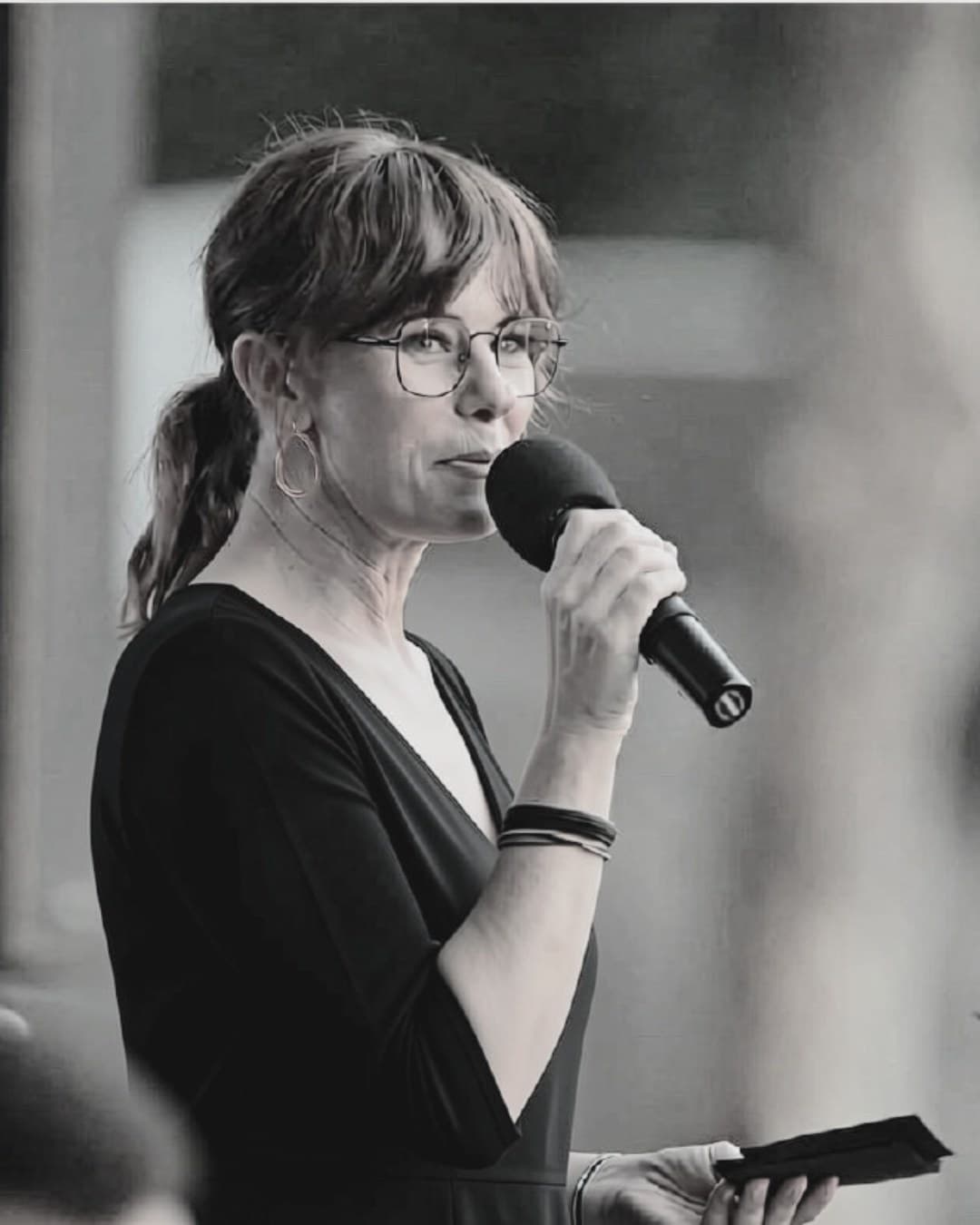 Milan Murray speaking into a handheld microphone, photographed in black and white.