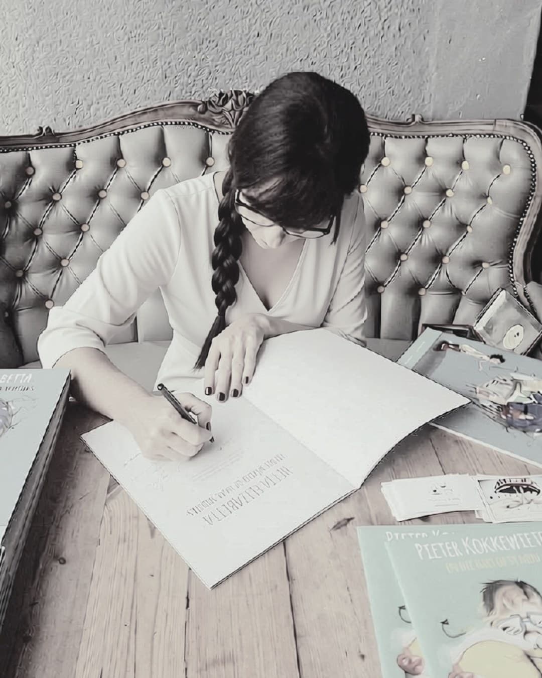 Milan Murray writing in a book at a wooden table, photographed in black and white.